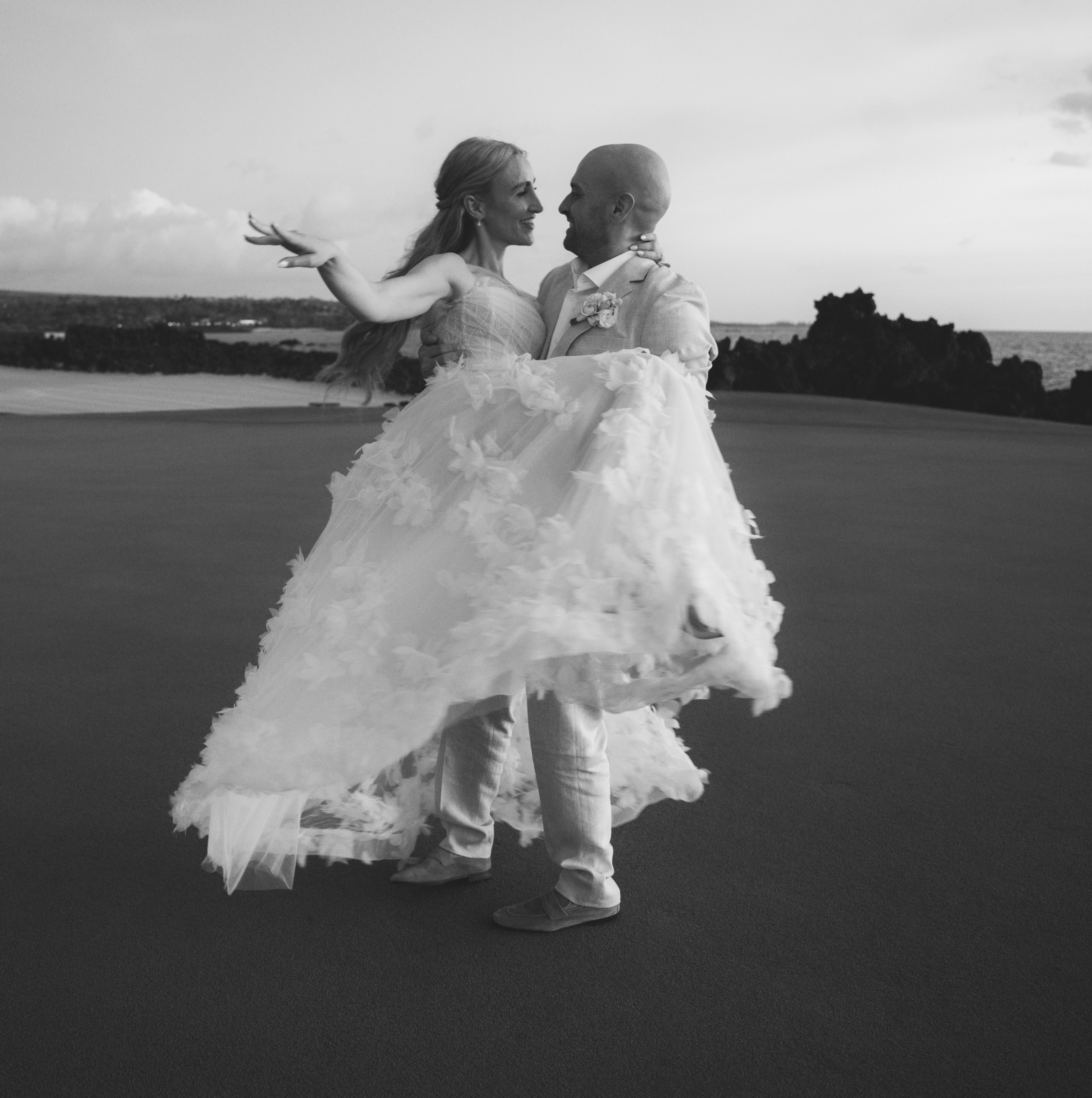 Black and white photo of groom lifting bride by the sea