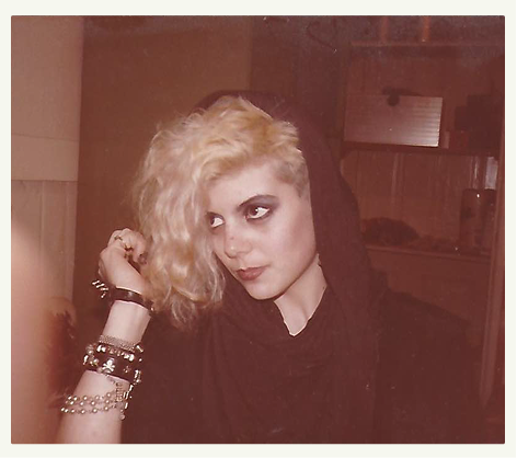 A sepia photograph for a young, blonde Ruby Dee Philippa wearing heavy eye makeup and a black hooded top.