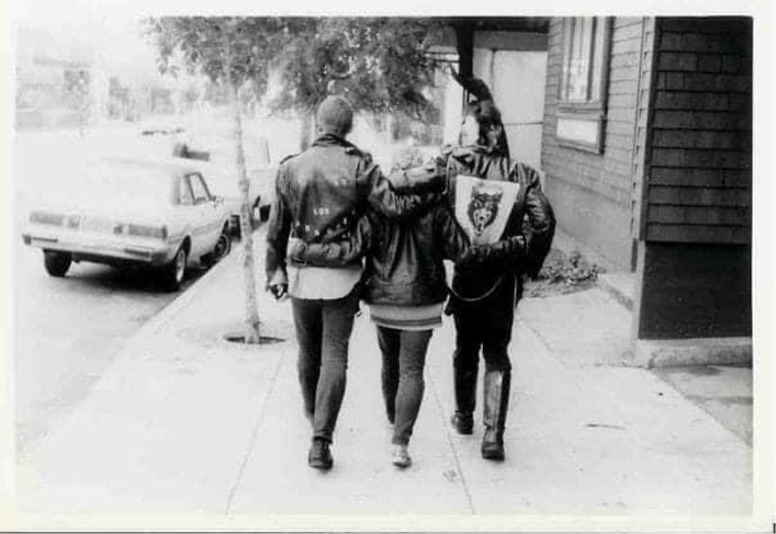 A black and white photograph of three punks walking down a city sidewalk.