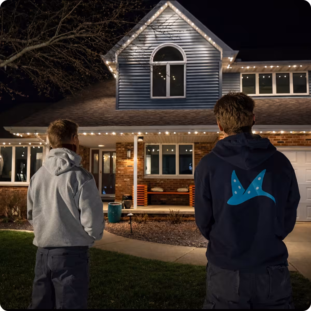 Max and Blake from Manta at an install of permanent lighting on a brick and blue shingle home