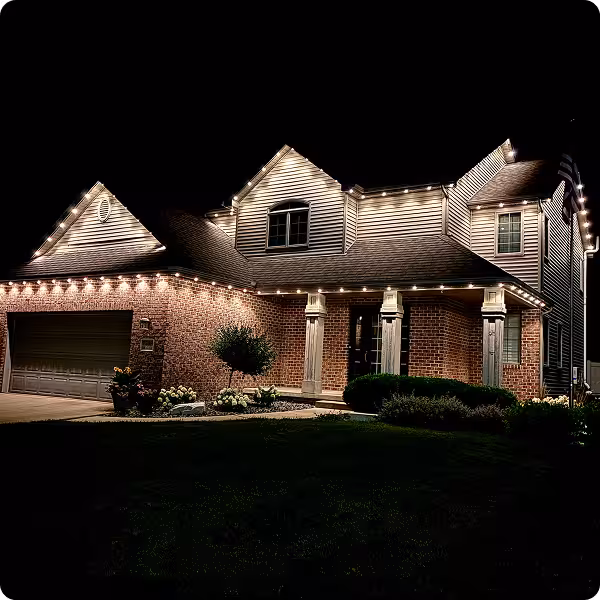 Manta permanent roofline lighting at night on a white house with dark roof from a side front angle