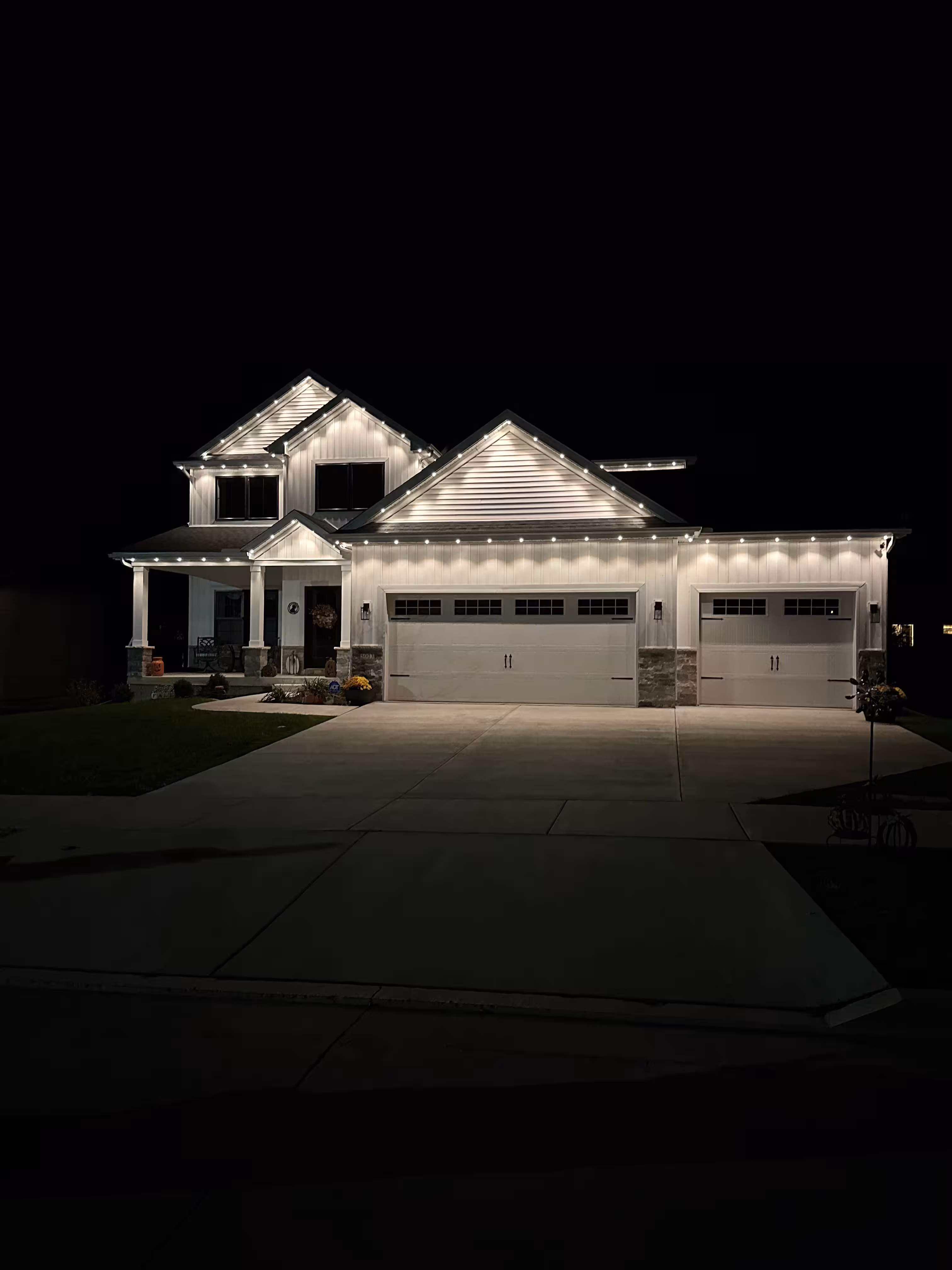 Front shot at night of a white home dark roof with permanent outdoor accent lighting