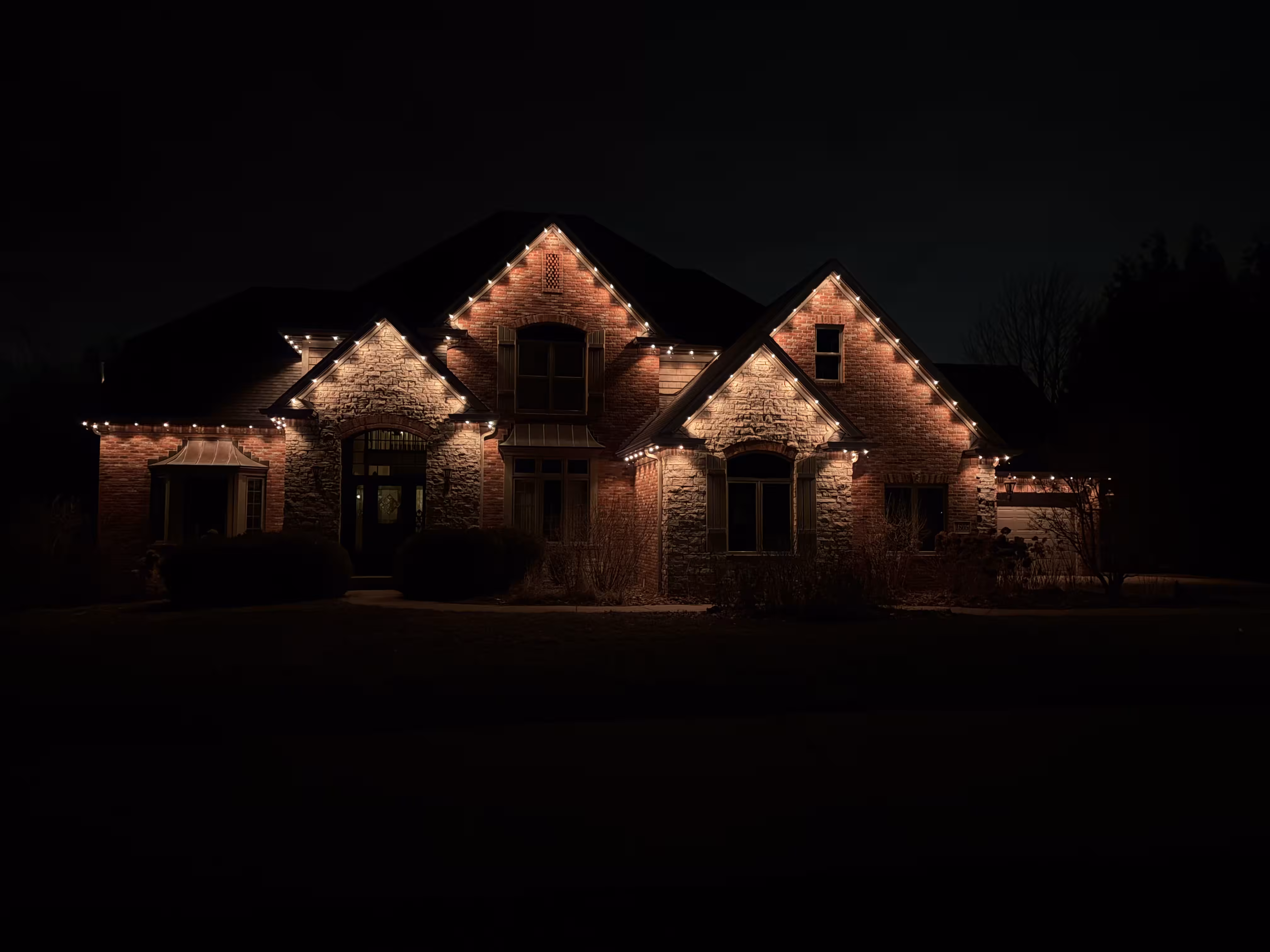 Front of a home at night with orange/white roofline lighting.