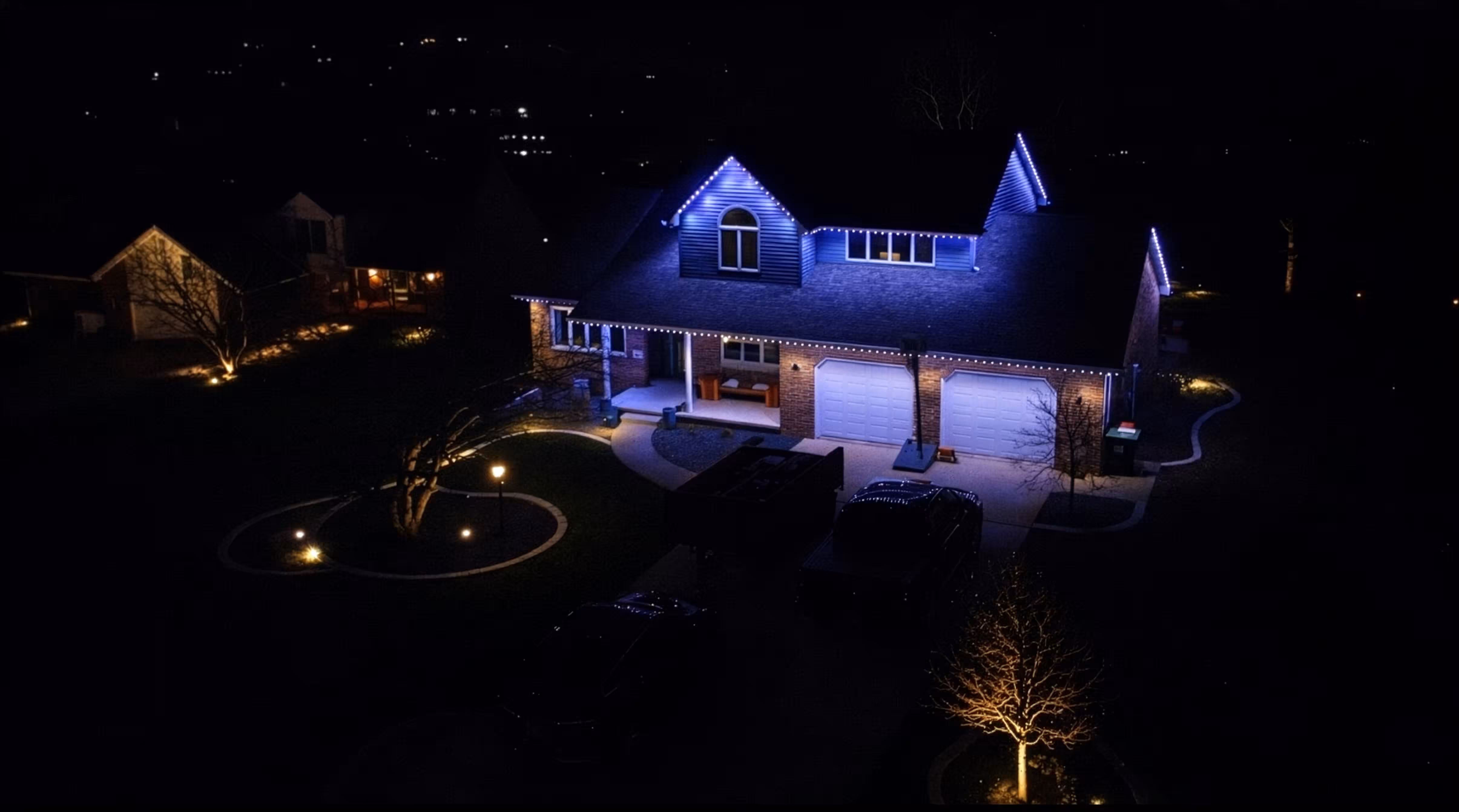 Drone shot of a home lit up with outdoor permanent accent lighting.