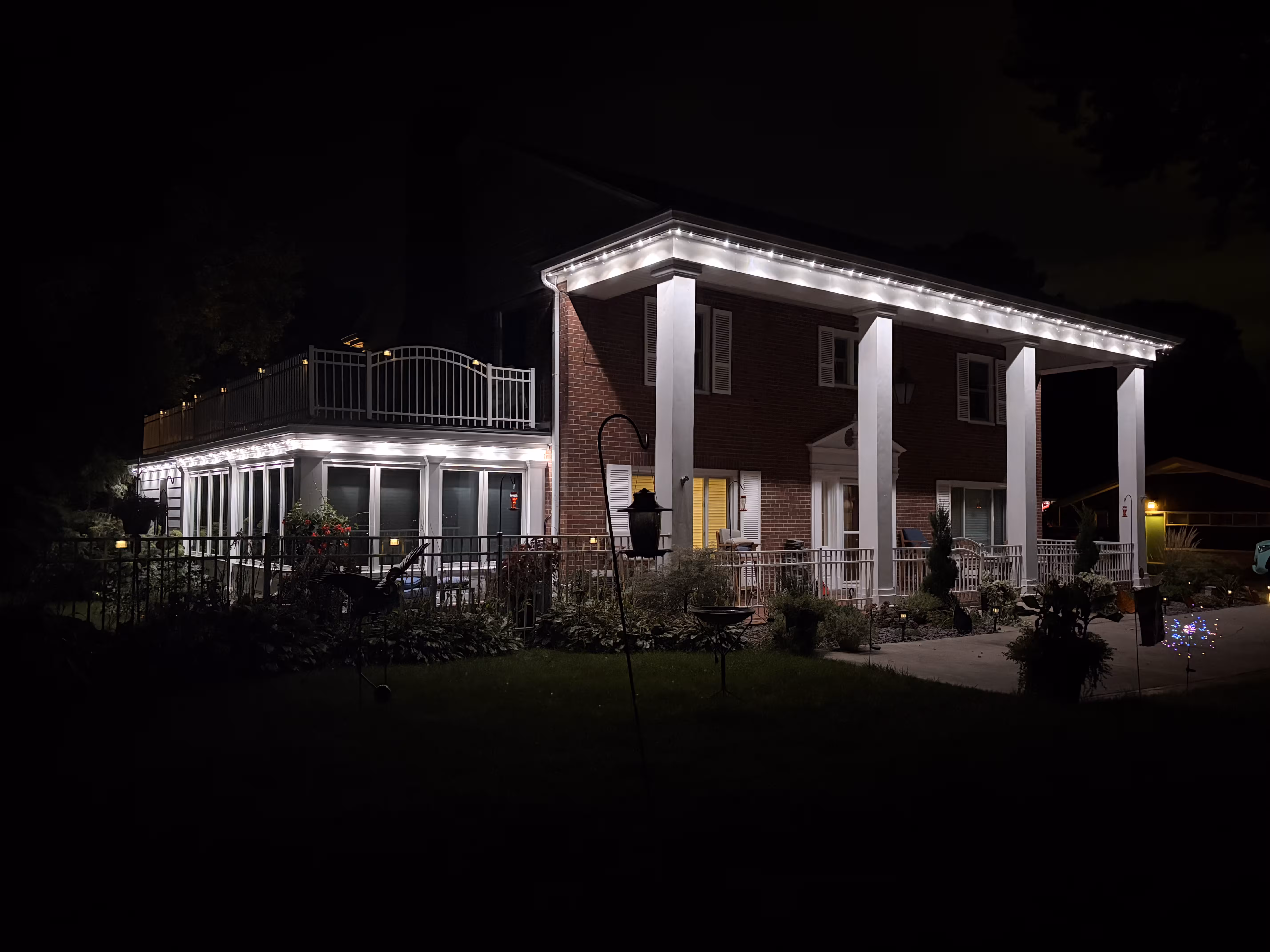 Night view of the front of a home with classic archways and columns being lit up by white permanent security lighting.