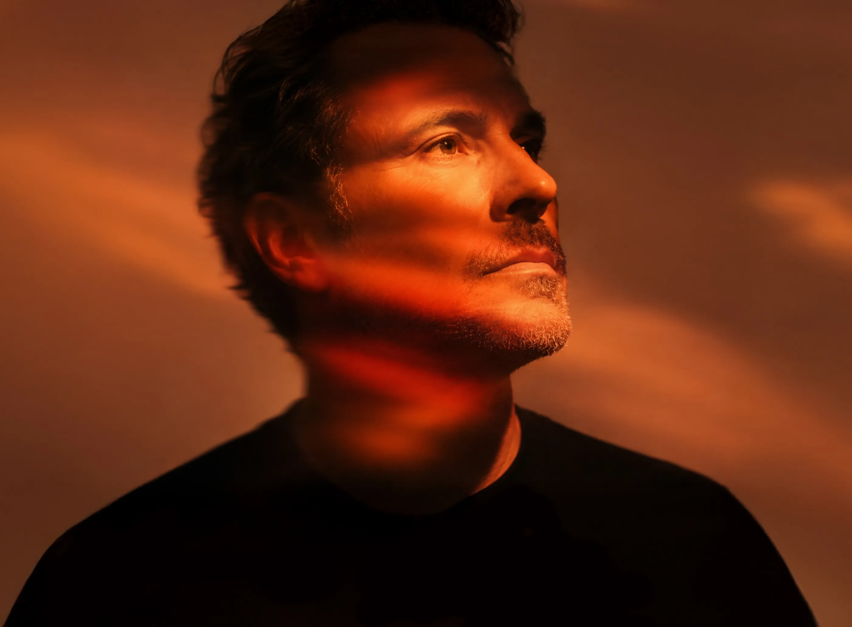 Close-up portrait of a man looking upward with warm red and orange light projected across his face