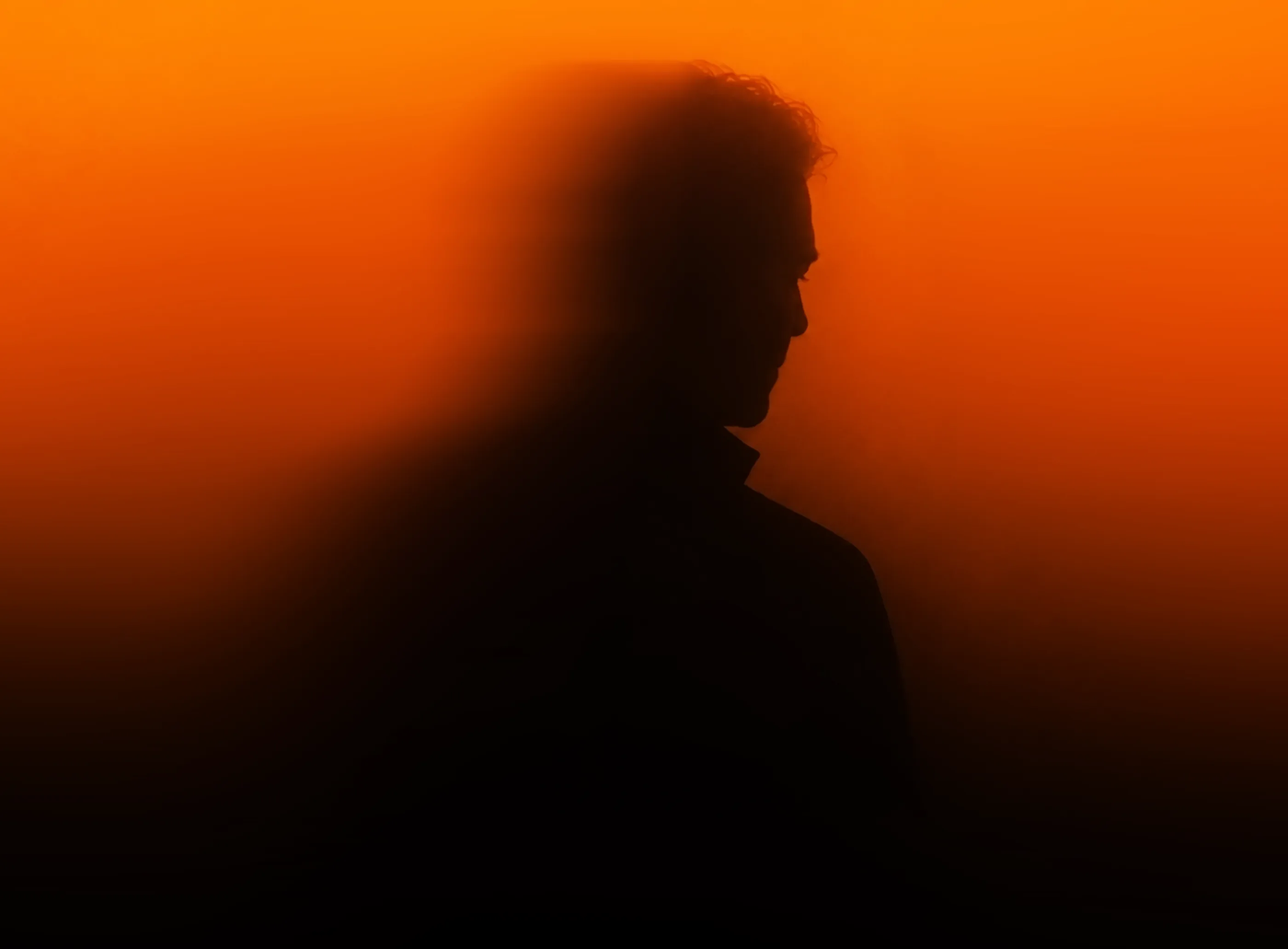 Blurred silhouette of a man standing against a vibrant orange illuminated background