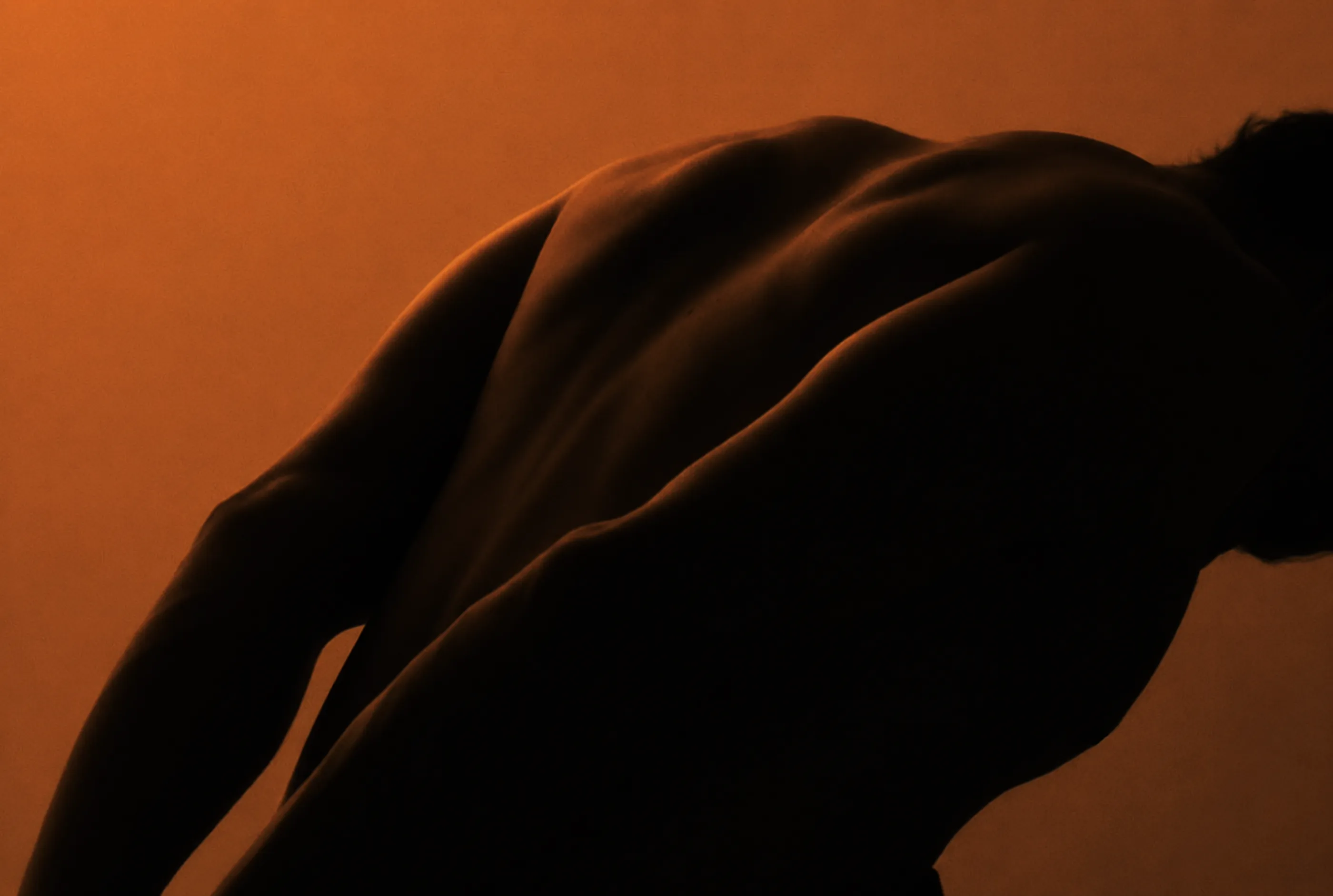 Dramatic silhouetted torso of a person flexing against a warm, backlit orange background
