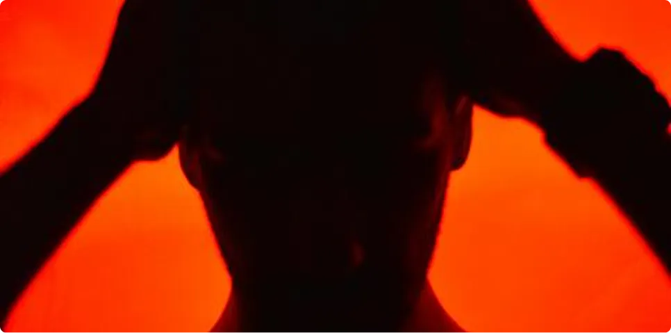 High-contrast silhouette of a person placing hands behind their head under intense red lighting