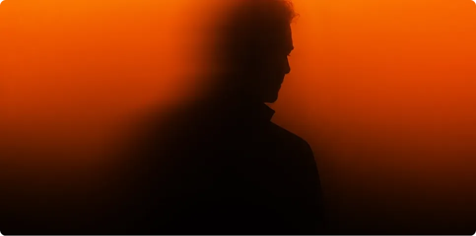 Silhouetted side profile of a person emerging through a warm orange backlit mist