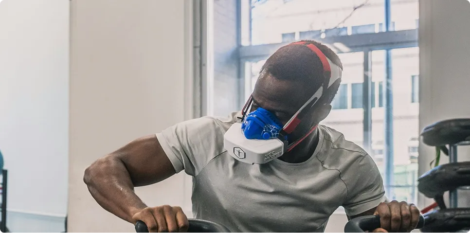Athlete performing cardio training on a stationary bike while wearing a oxygen intake mask