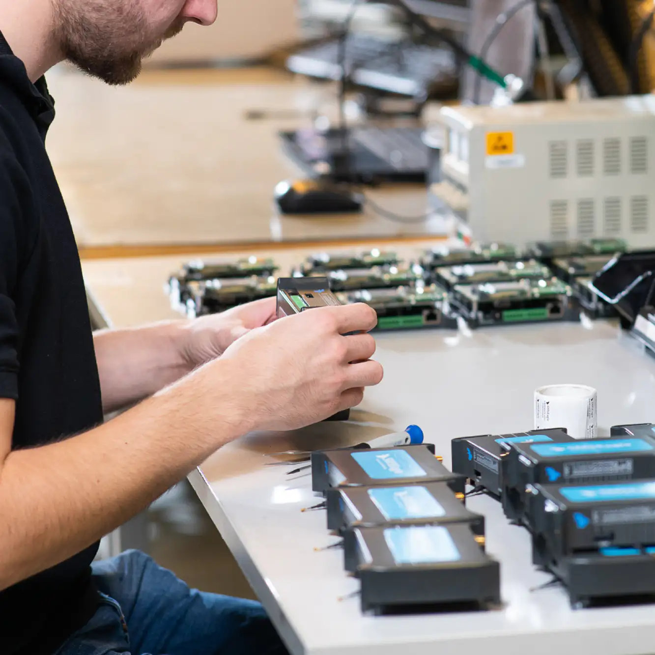 Mężczyzna trzyma urządzenie elektroniczne przy stole z wieloma podobnymi komponentami.