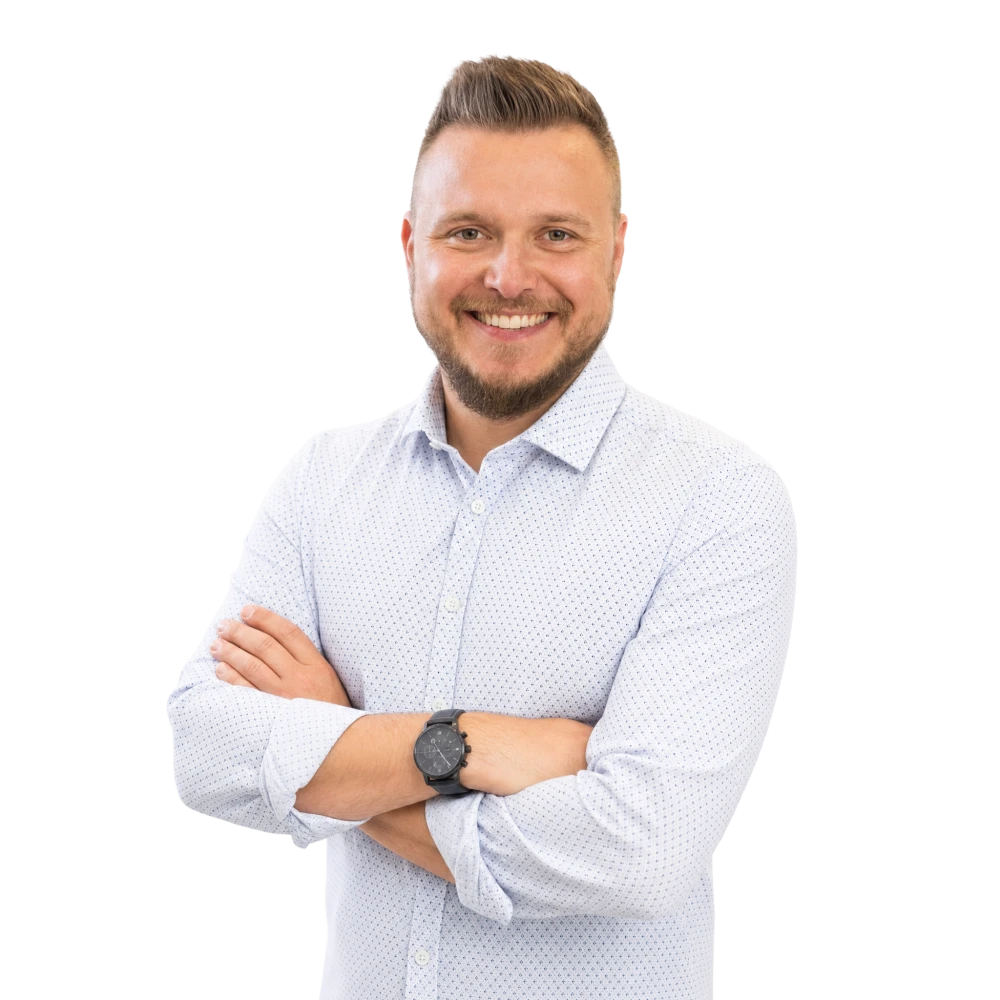 Uśmiechnięty mężczyzna z krótkimi włosami w jasnej, wzorzystej koszuli z zegarkiem na ręku.