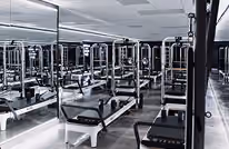 Modern Pilates studio with multiple reformer machines lined up in rows, surrounded by mirrored walls and a clean, minimalistic design.