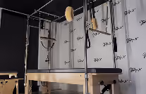 A trapeze apparatus with a suspended bar and safety net in a studio with a branded backdrop.
