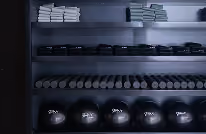 Rows of dumbbells and weights neatly arranged on a gym rack in a dimly lit setting.