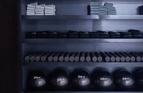 Shelves in a gym holding neatly folded towels on the top shelf, stacked black weights on the middle shelves, and large medicine balls on the bottom shelf.