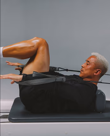 Man with short gray hair performing an exercise using resistance bands while lying on a padded bench, pulling bands connected to his hands with his knees bent.