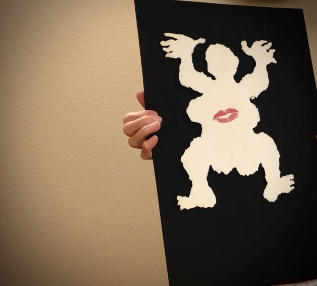Dancing figure torn out of white cardboard on black background. Kiss mark on belly of figure.