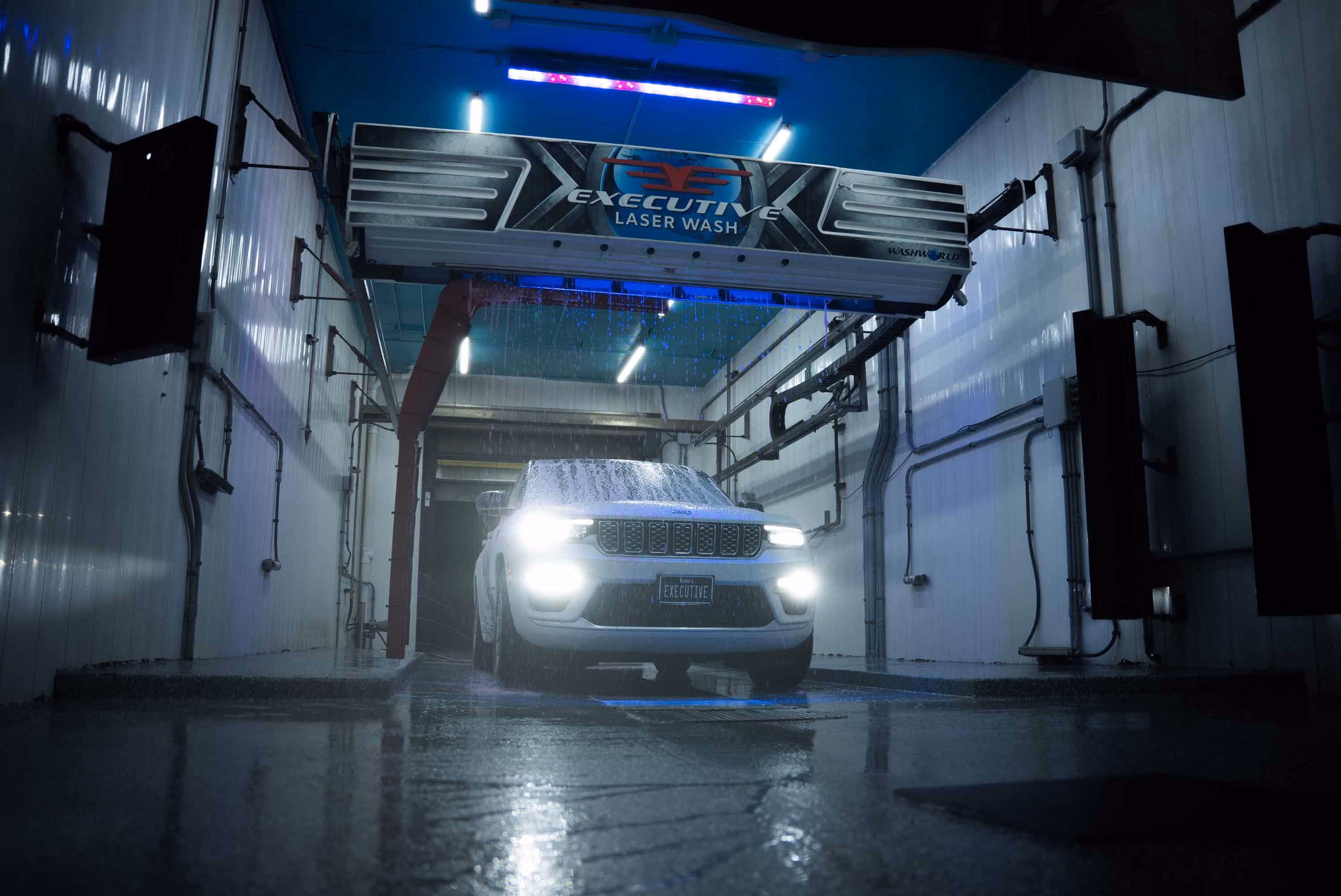 White SUV with headlights on inside an Executive Laser Wash car wash system.