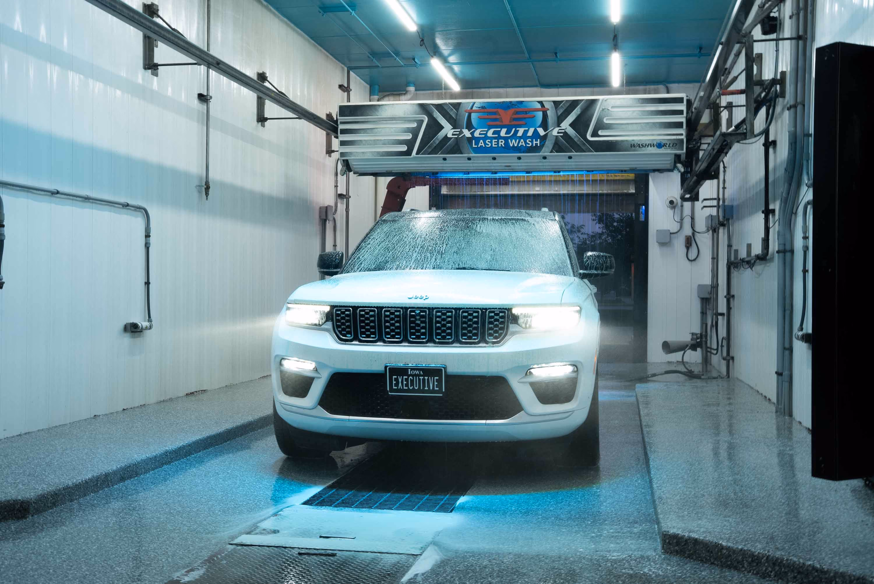 White Jeep SUV with headlights on undergoing a laser wash inside Executive Laser Wash bay.