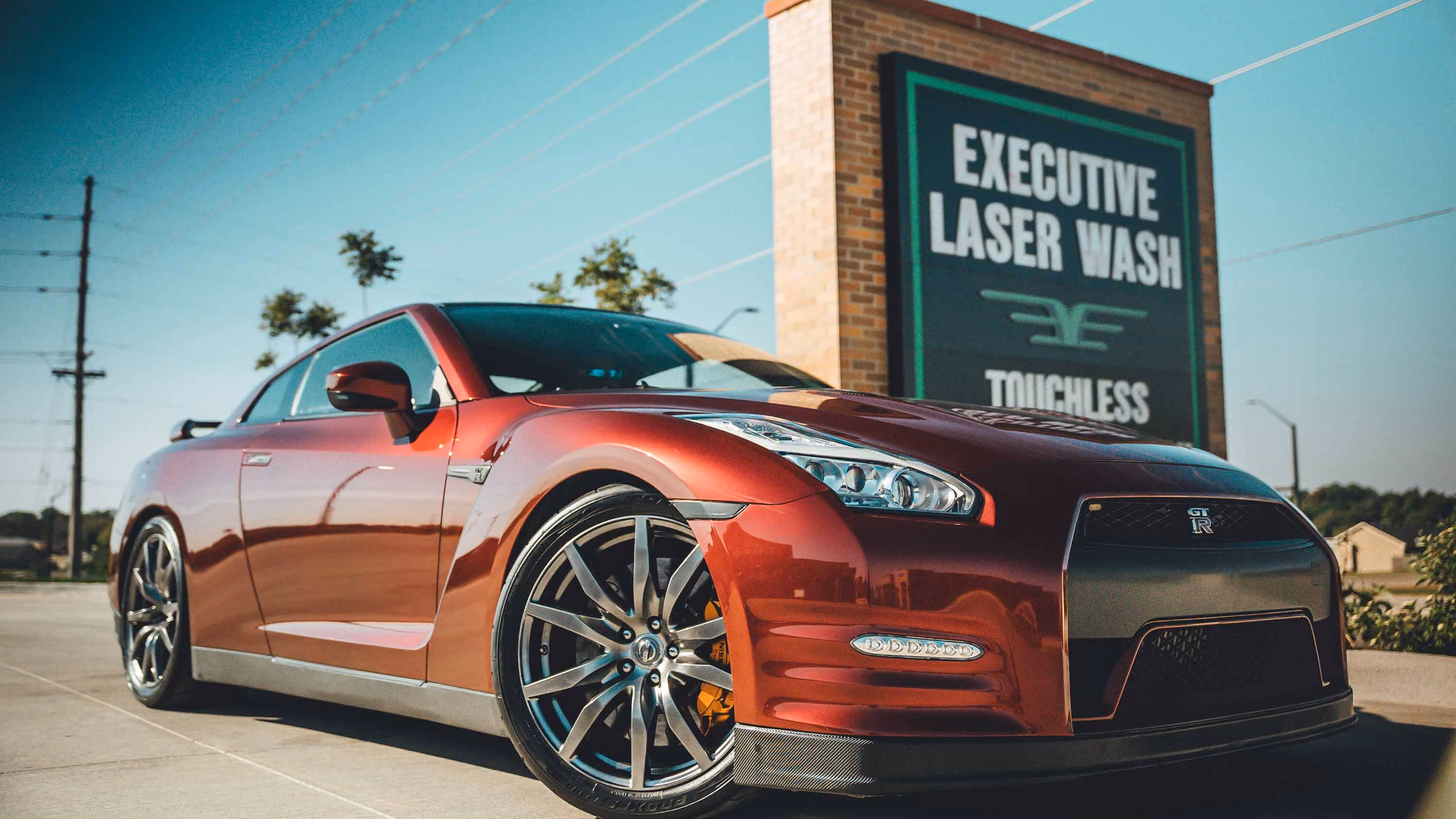 Red Nissan GT-R parked in front of a brick sign reading Executive Laser Wash touchless automatic wash.