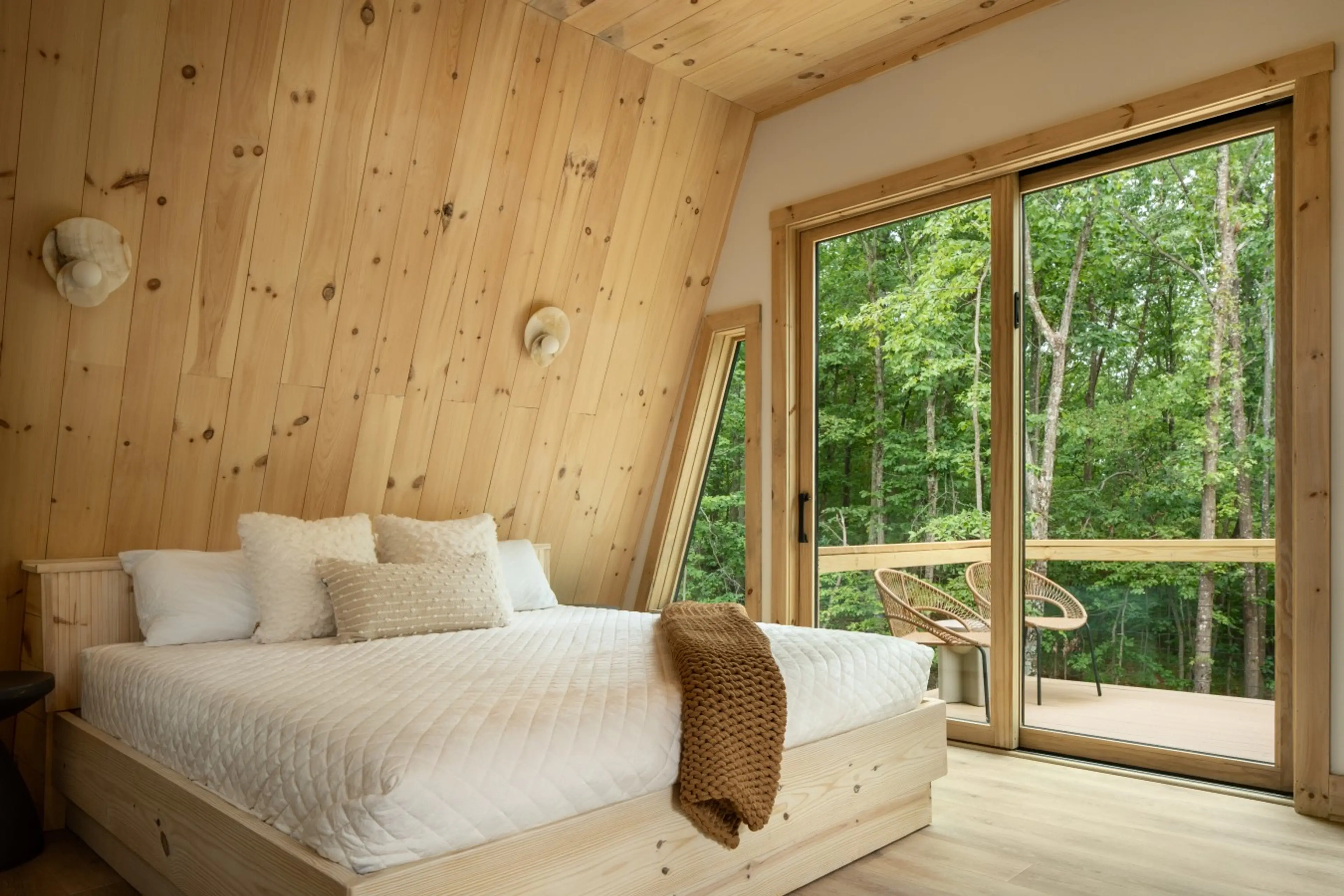 Primary bedroom at Solhaus Shenandoah with a glass wall opening to the deck and forest view