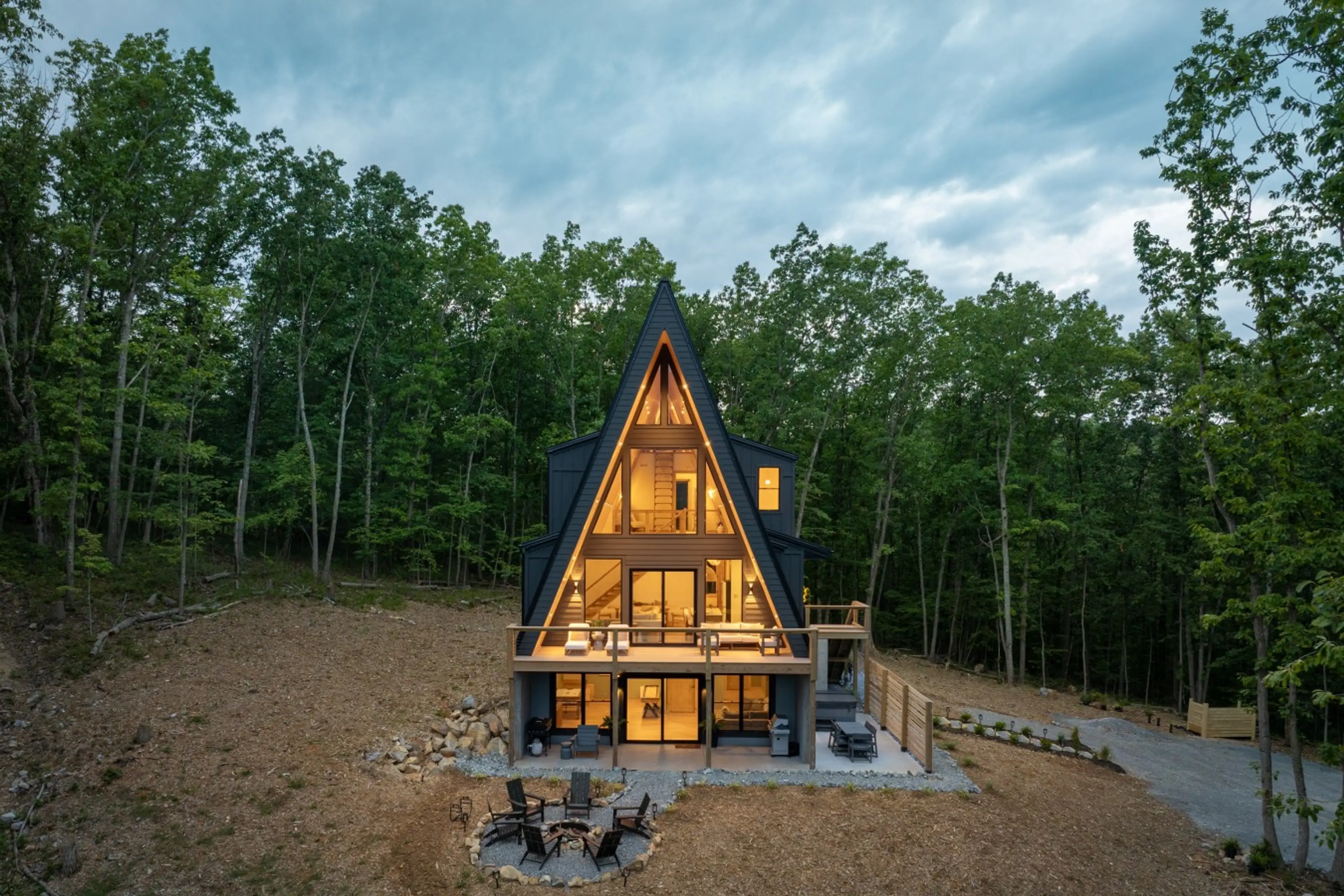 Solhaus Shenandoah A-frame cabin lit up at twilight in a wooded clearing