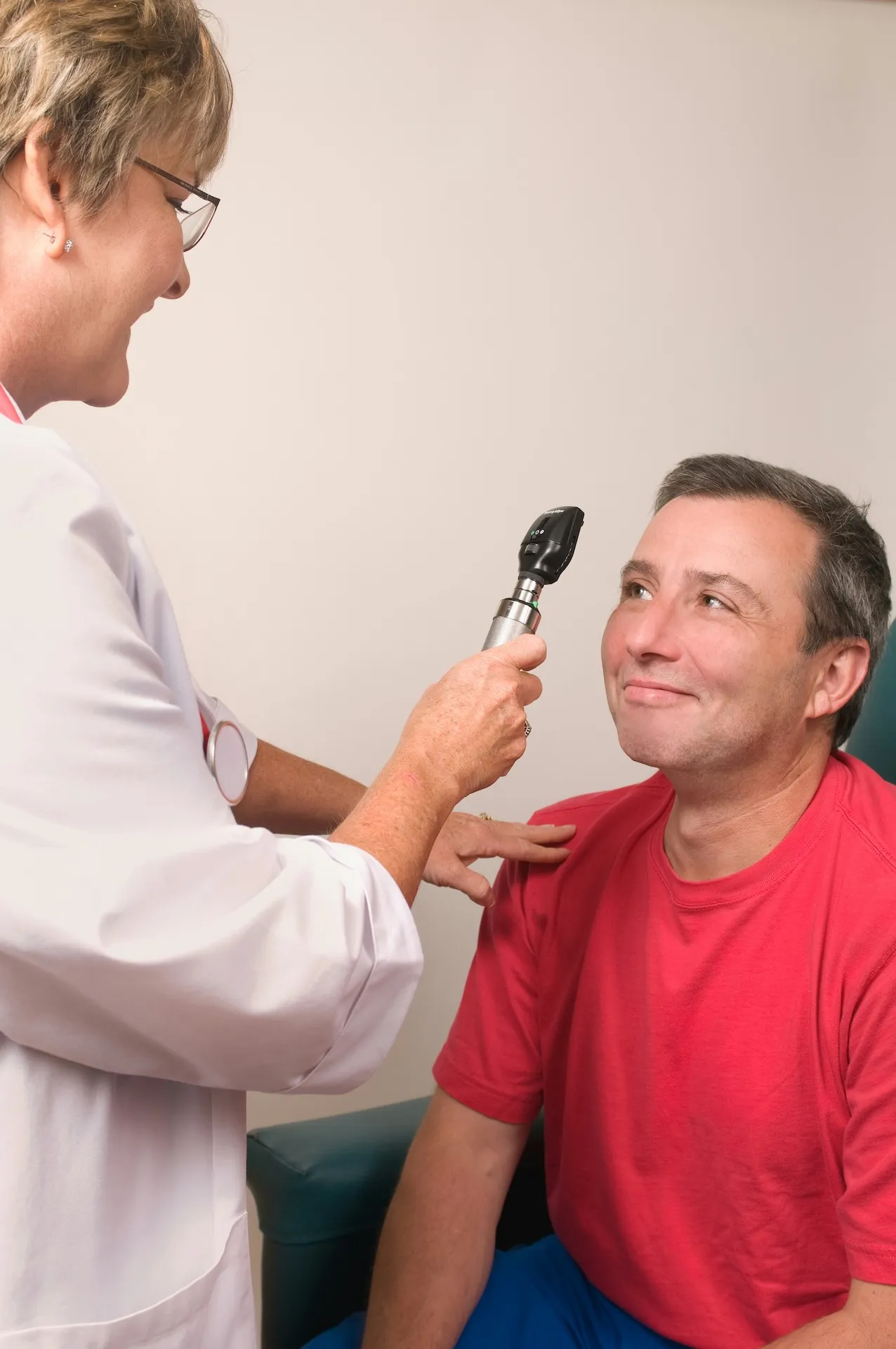 Doctor using otoscope to examine smiling man's ear in a clinical setting.