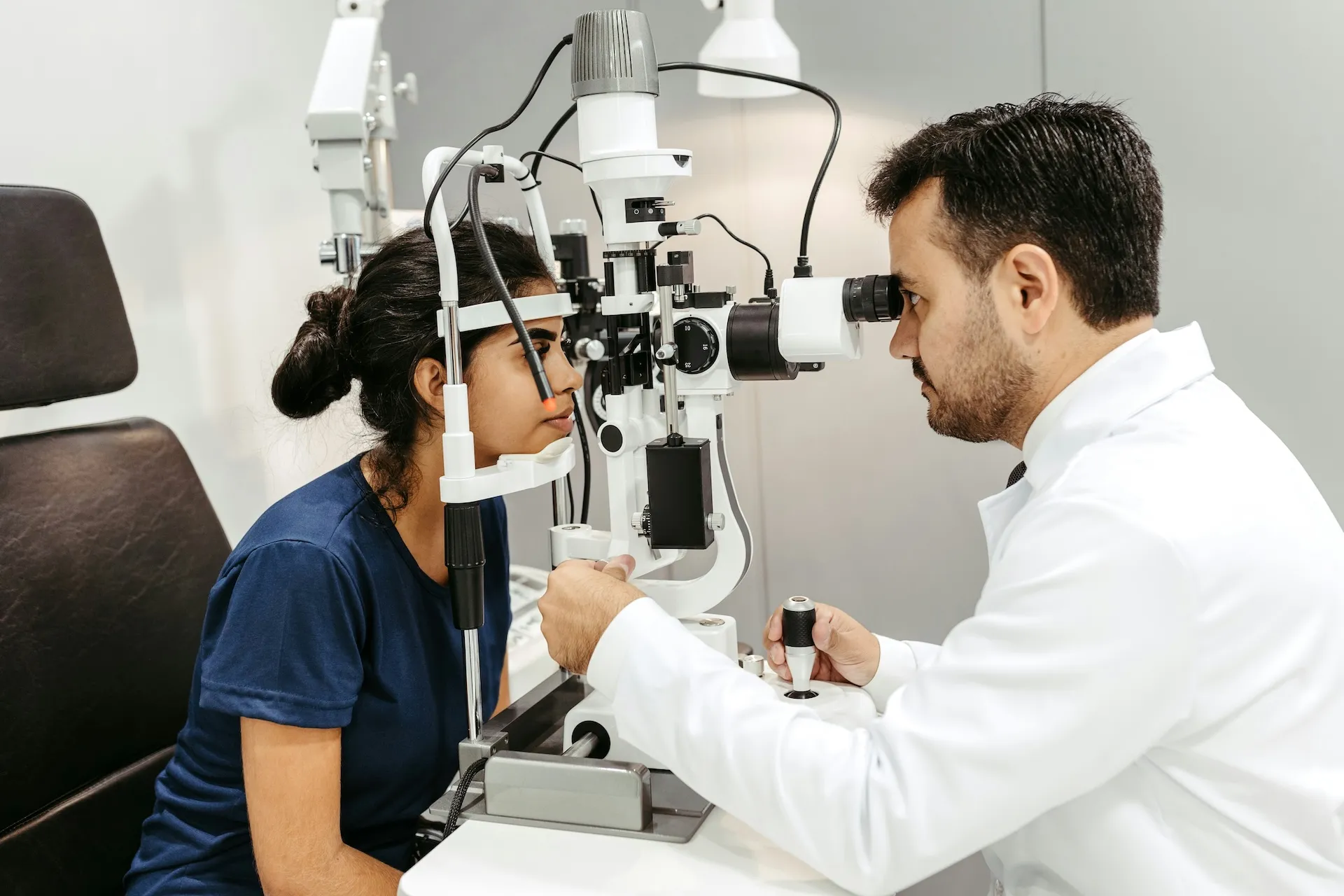 Optometrist examining young woman’s eyes using slit lamp in a clinical setting.