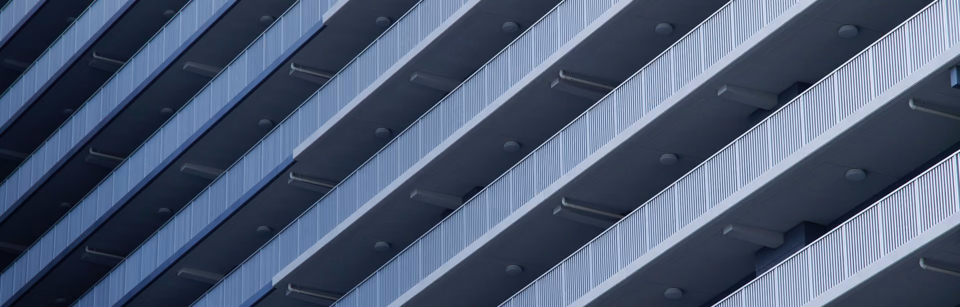 Close-up of a modern building facade showing several floors with uniform balconies featuring vertical metal railings and ceiling lights.
