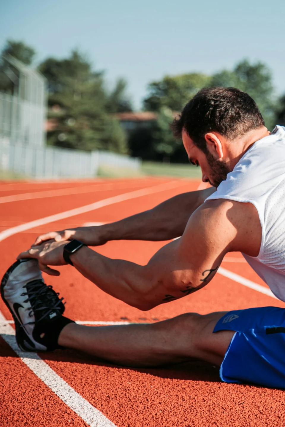 Athlete stretching his hamstrings on a running track, representing sports performance training at Lumen Athletics in Cheyenne, WY.