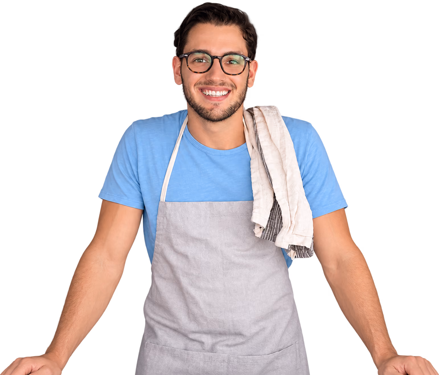 Joven sonriente con gafas, camiseta azul y delantal gris, con una toalla colgada en el hombro, apoyado con ambas manos hacia adelante.