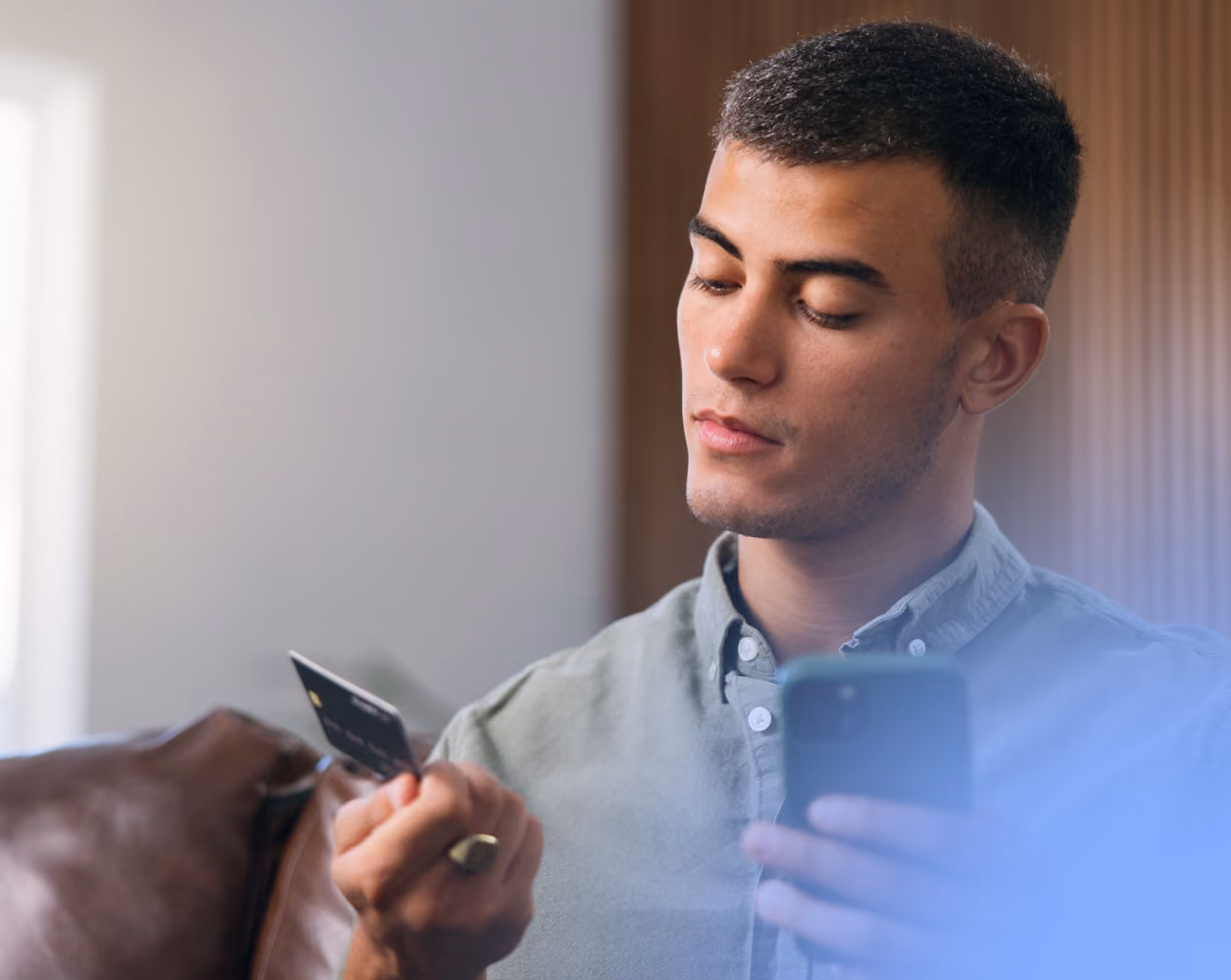 Hombre joven en una mano tiene su tarjeta de crédito y en la otra su celular.