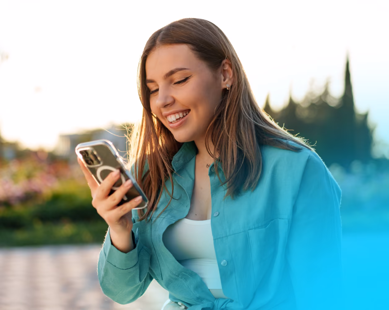 Mujer sonriente usando un teléfono celular mientrasen un parque.