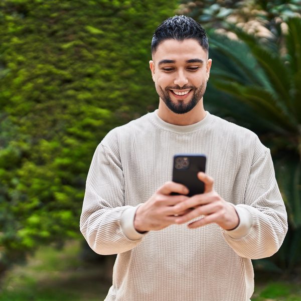 Hombre joven sonriendo mientras usa su celular en un parque