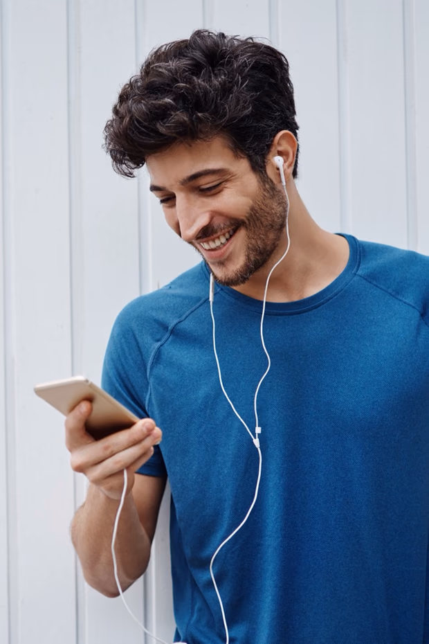 Hombre sonriendo con auriculares mientras usa el celular