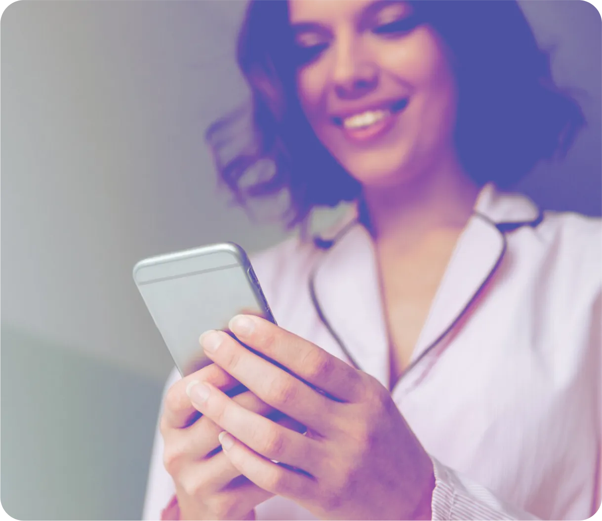 Smiling woman in light-colored pajamas holding and looking at a smartphone.