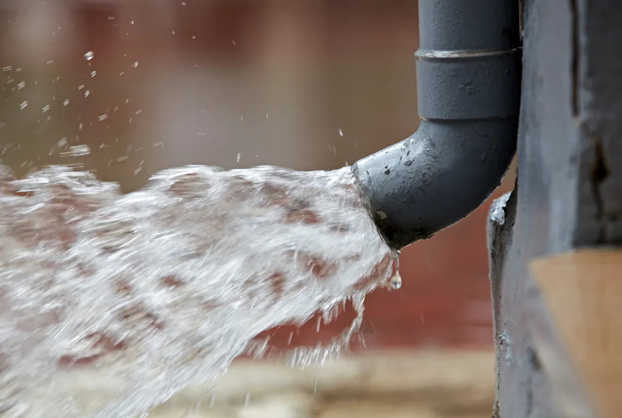 Close-up of water forcefully flowing out of a grey metal pipe attached to a concrete wall.