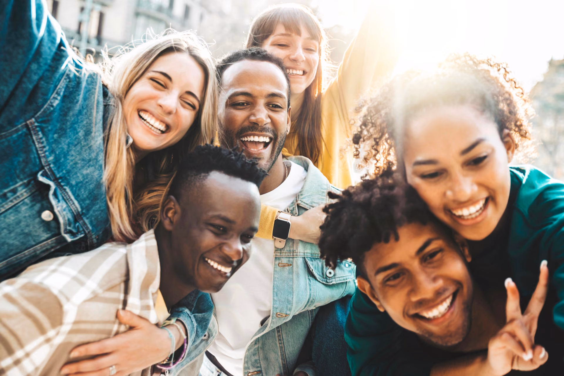 Group of six diverse young adults smiling, laughing, and enjoying a sunny outdoor moment together.