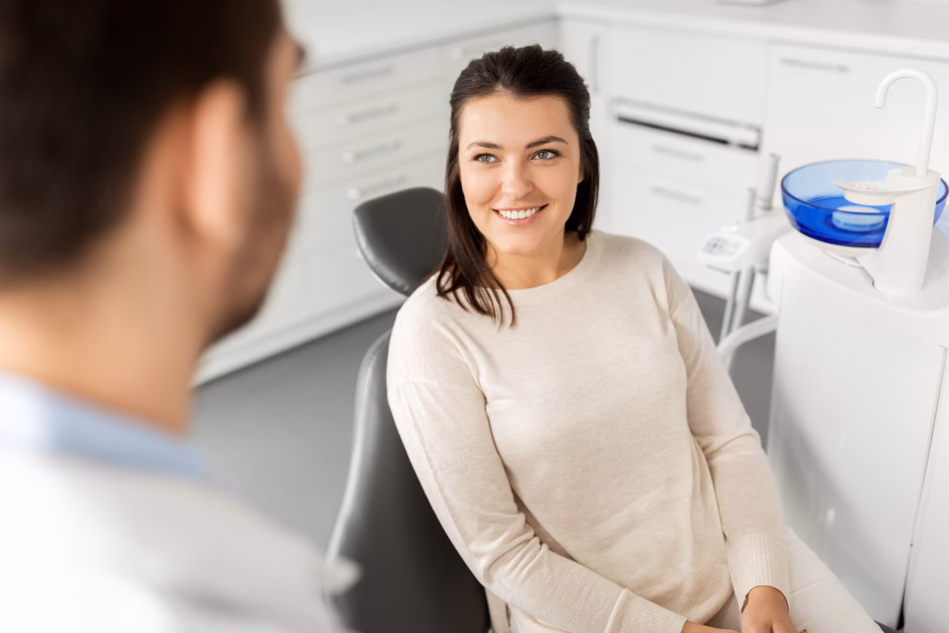 Smiling woman sitting in a dentist's chair talking with a dentist in a dental clinic.