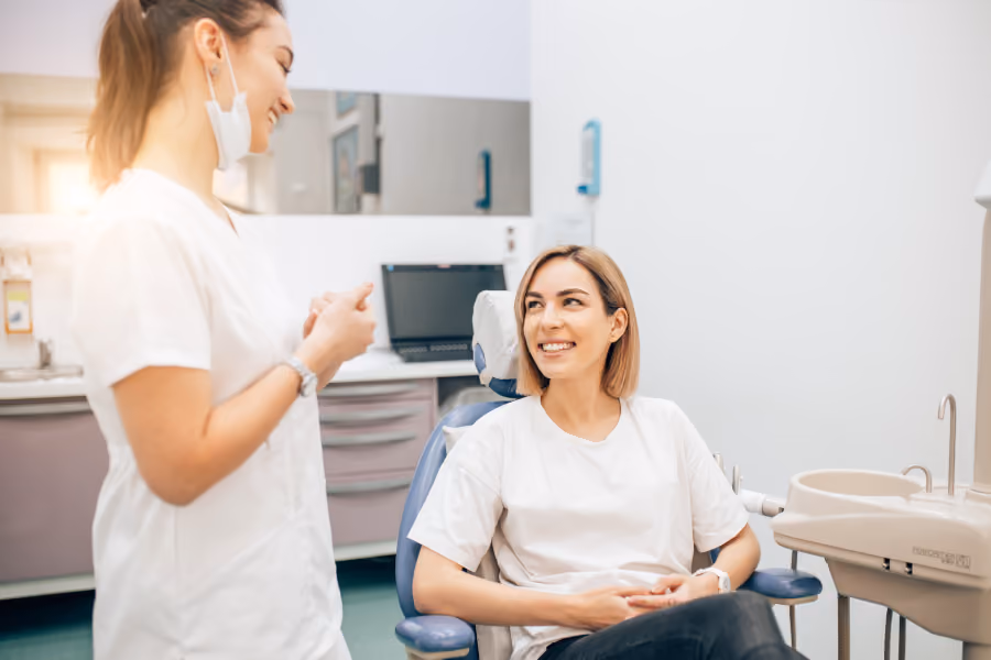 Patient sitting in dental chair smiling at female dentist standing nearby in clinic room.