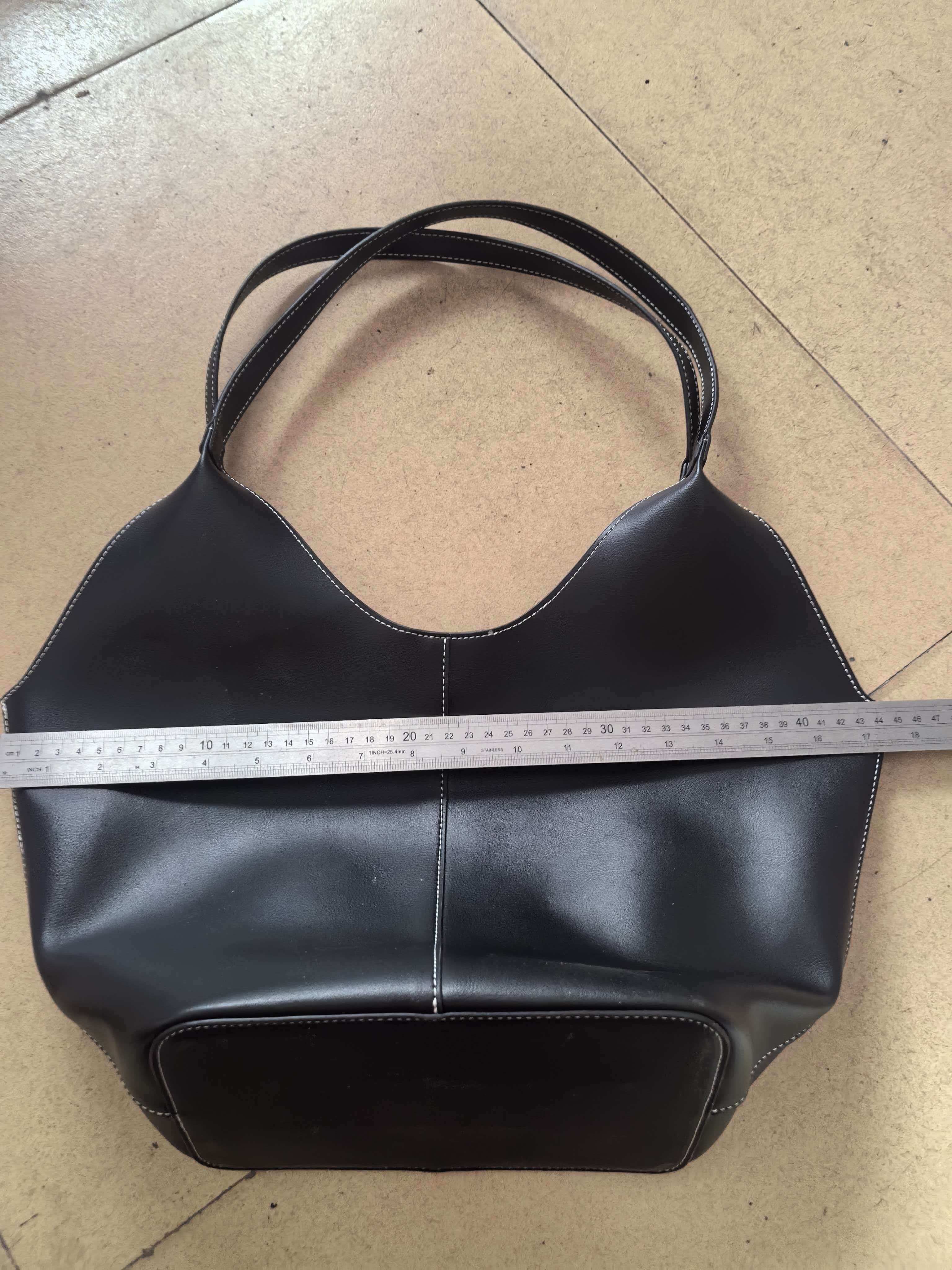 Side profile view of black handbag showing strap and structured design