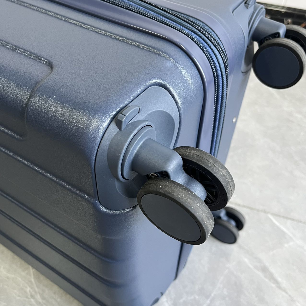 Bottom corner detail of blue luggage showing double spinner wheels