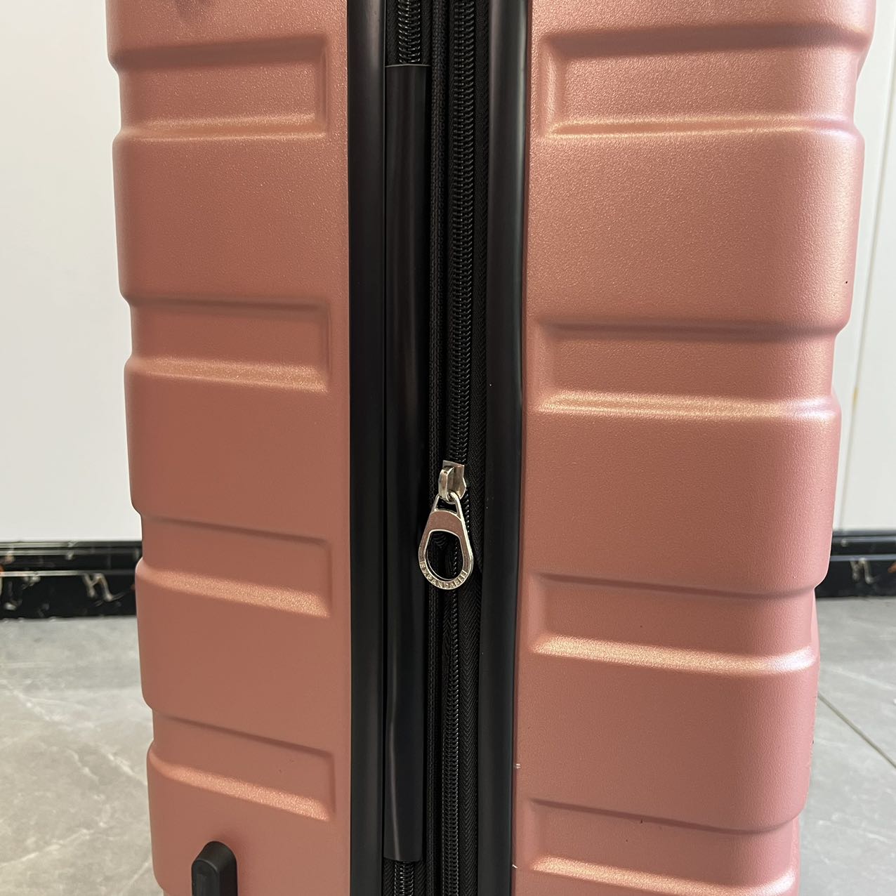 Detail view of zipper closure and side lock on rose gold luggage