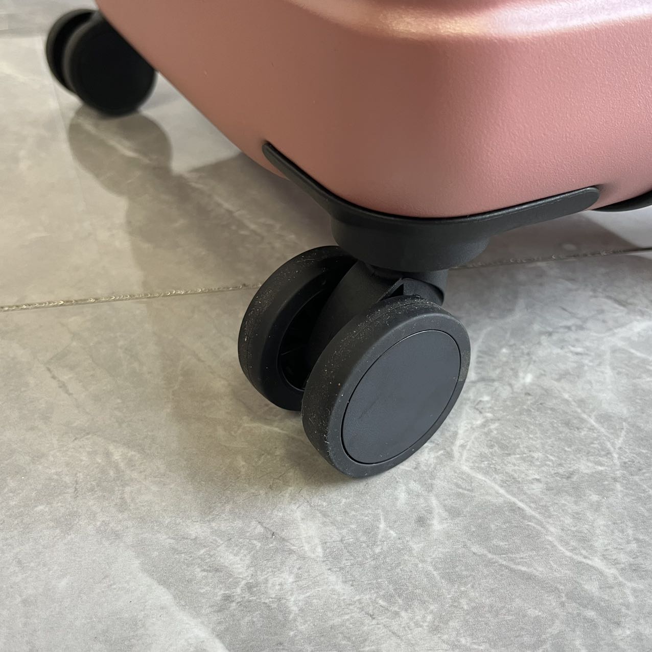 Close-up view of double 360-degree spinner wheels on rose gold luggage