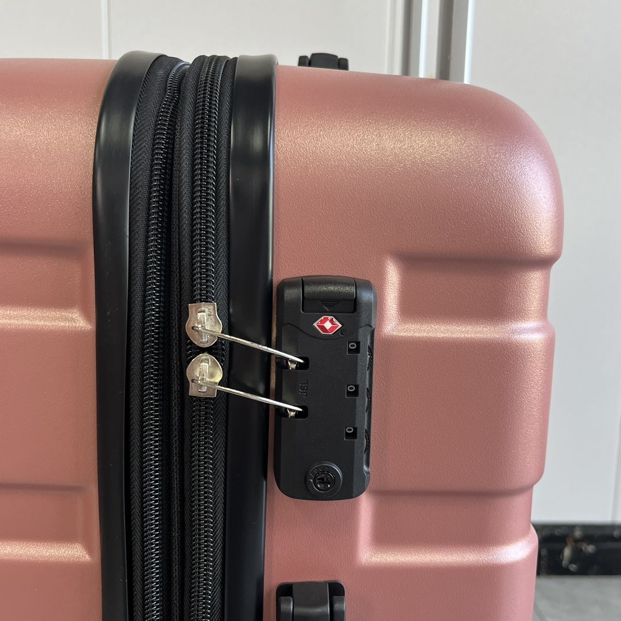 Side view detail of rose gold hard-shell luggage showing side handle and feet