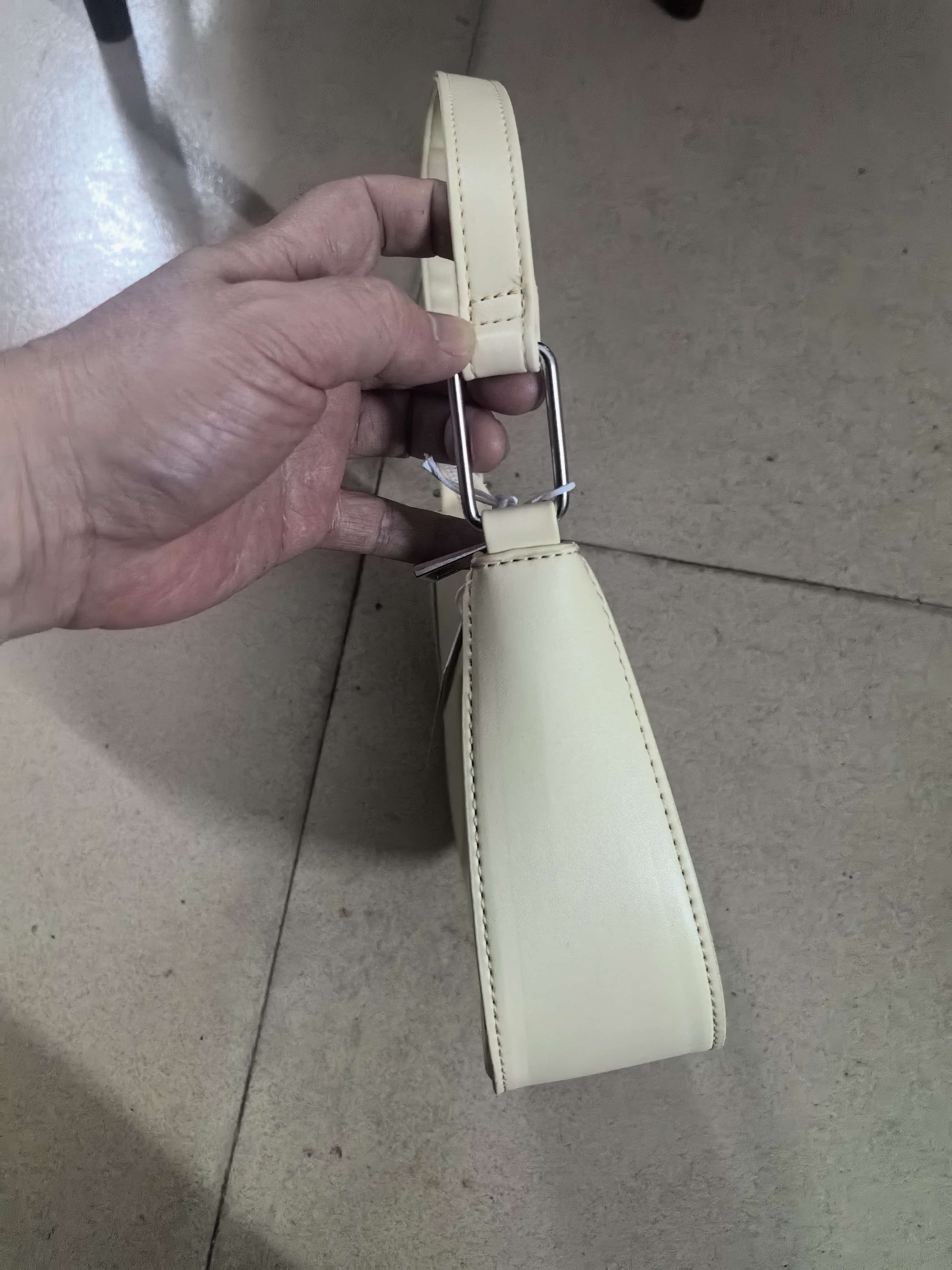 Hand holding cream leather hobo bag by its shoulder strap