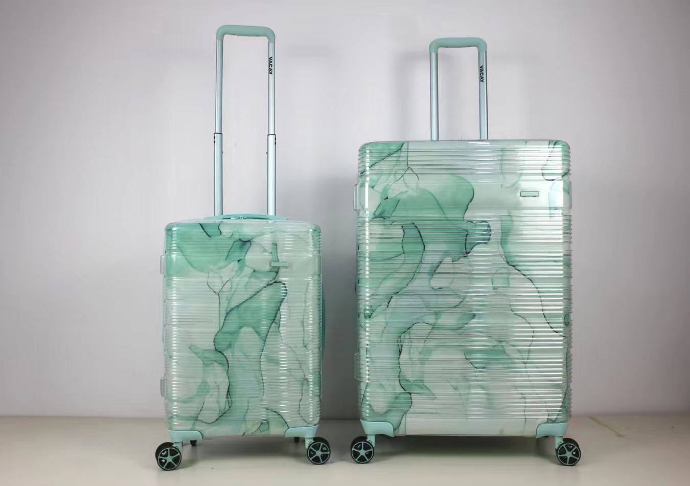 Side perspective view of green patterned trolley suitcases in two sizes