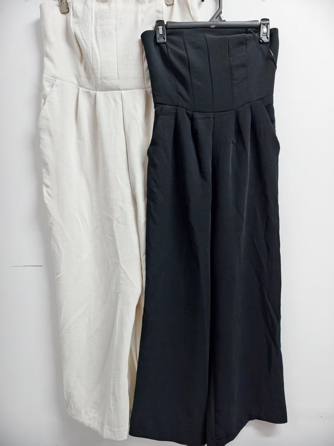 Black and off-white ladies' strapless jumpsuits displayed together on clothing rack